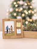 A rectangular bamboo photo frame with a photo insert and a small cork notepad holder, styled on a tabletop with a blurred Christmas tree and succulents in the background. - Image 