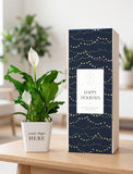 A tall rectangular gift box with a navy blue holiday design featuring gold string lights and dots, standing on a light wood table next to a potted peace lily in a white pot with the text 'your logo HERE'. - Image 