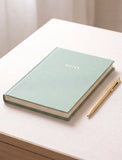 A mint green hardcover notebook with the word 'NOTES' in gold foil on the cover, placed on a light beige tabletop next to a gold pen. - Image 